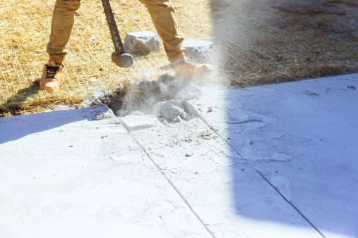 Hammer wielding worker breaks concrete driveway at construction site